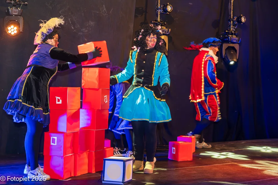 Twee Pieten spelen bij een stapel cadeaus op het podium in 2025.